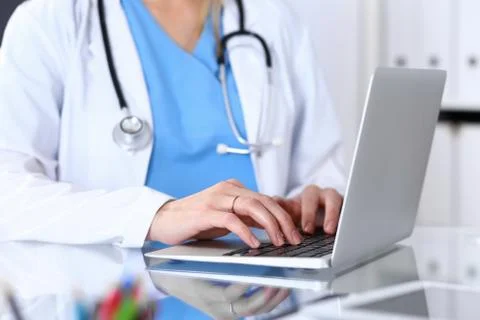 Doctor typing on laptop computer while sitting at the glass desk in hospital Stockfoto's