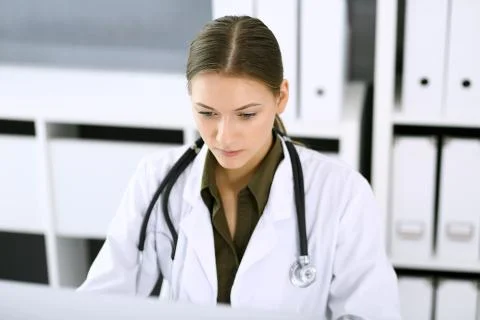 Doctor typing on pc computer while sitting at the desk in hospital office Foto stock