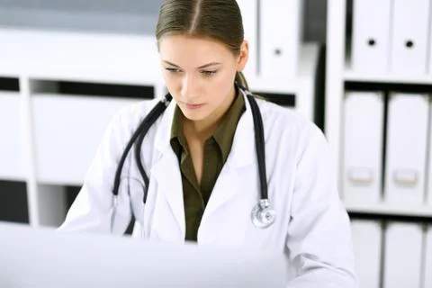 Doctor typing on pc computer while sitting at the desk in hospital office Stock Photos