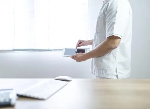 Doctor in the uniform using computer tablet next to his office desk in hospital Stock Photos