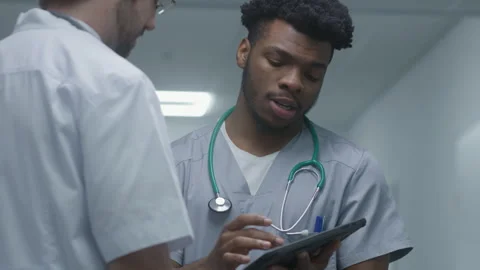 Doctor uses digital tablet computer, shows diagnostic results to colleague Stock Footage 249789931