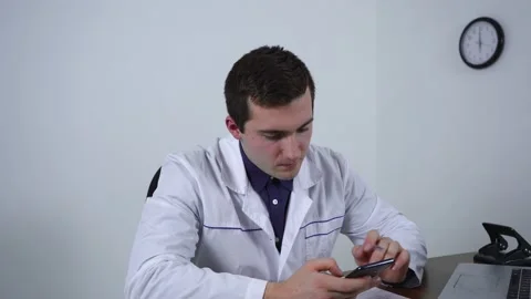 The doctor uses the phone while sitting at the table Stock Footage 145220969