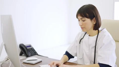 Doctor using computer sitting on a desk in a clinic Stock Footage 267538973