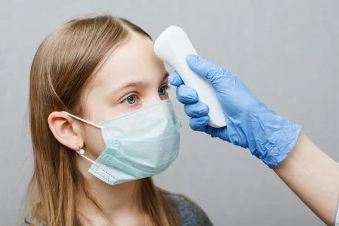 Doctor using infrared thermometer checking body temperature of a girl wearing Stock Photos