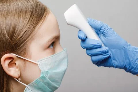 Doctor using infrared thermometer checking body temperature of a girl wearing Stock Photos