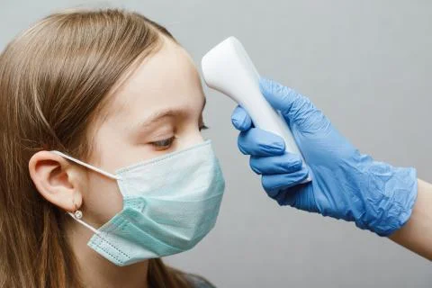 Doctor using infrared thermometer checking body temperature of a girl wearing Stock Photos