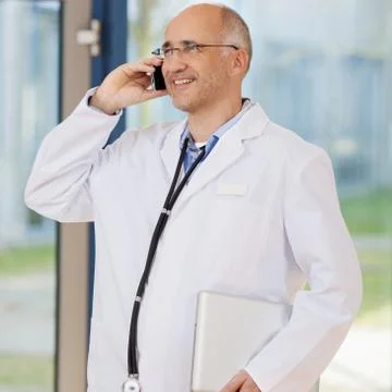 Doctor using mobile phone while holding laptop Stock Photos