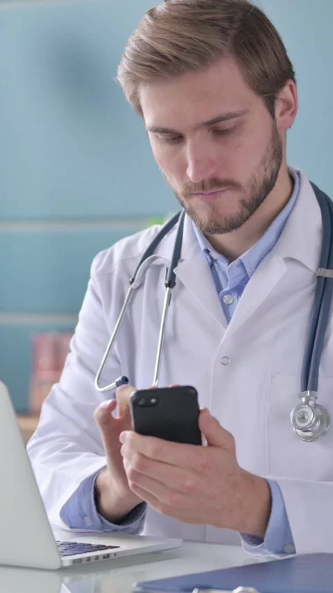 Doctor using Smartphone while Working on Laptop in Office, Vertical Video Stock Footage 339580014