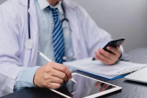 Doctor using tablet and smartphone while taking notes in a clinical setting Stock Photos