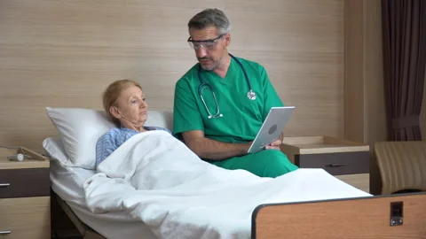 Doctor using tablet computer  discussing with senior woman patient lying on b Stock Footage 159710826