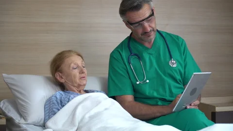 Doctor using tablet computer  discussing with senior woman patient lying on b Stock Footage 159711369