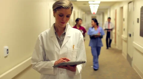 Doctor Walking Along Hospital Corridor Using Digital Tablet Stock Footage