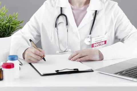 A doctor in a white coat makes a note on paper with a pen. Stock Photos