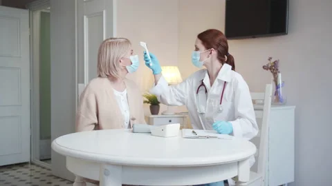 A doctor in a white coat puts a thermometer on the patient's forehead and shows Stock Footage 173941006