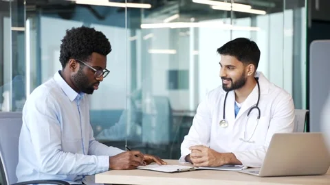 Doctor in white coat showing document to patient sitting at desk in hospital  Stock Footage 329052221