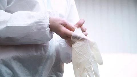 The doctor in white suit puts protective gloves on dark background Stock Footage