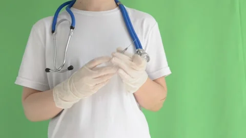 A doctor without a face in gloves holds a syringe on a green background, mono Stock Footage 201856845