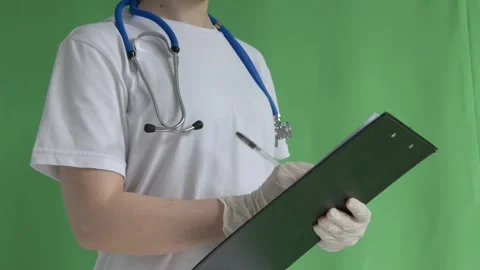 A doctor without a face in gloves signs papers on a tablet on a green backgro Stock Footage 201639008
