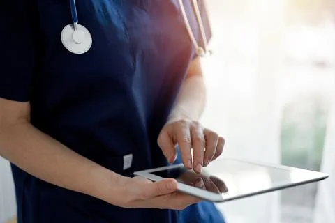 Doctor woman using tablet computer while standing near panorama window in clinic Stock Photos