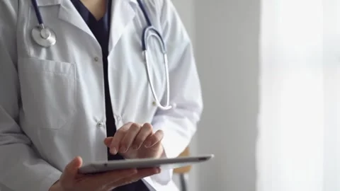 Doctor woman at work using a tablet computer while standing near panorama window Stock Footage 244575856