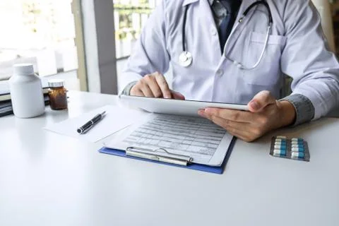 Doctor working and using digital tablet note information on paper report in h Stock Photos