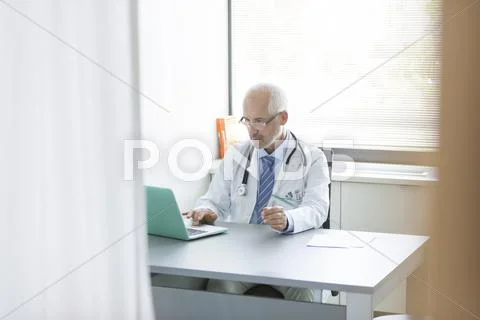 Doctor Working At Laptop In Doctor's Office