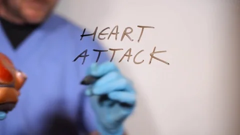 Doctor writes heart attack on a clear screen holding a model of a heart Stock Footage 79334506