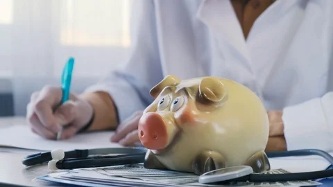 The doctor writes something against the backdrop of a piggy bank and money Stock Footage 118848934