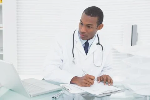 Doctor writing a note while using computer at medical office 库存照片