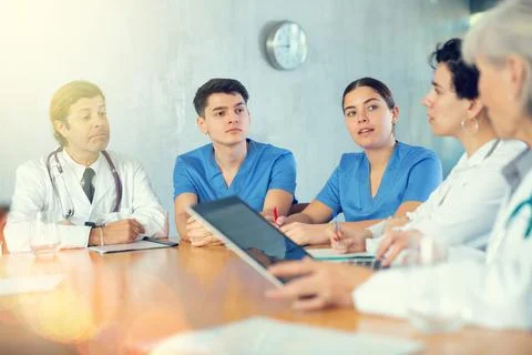 Doctors and nurses of different ages discussing topic of day while sitting at Stock Photos