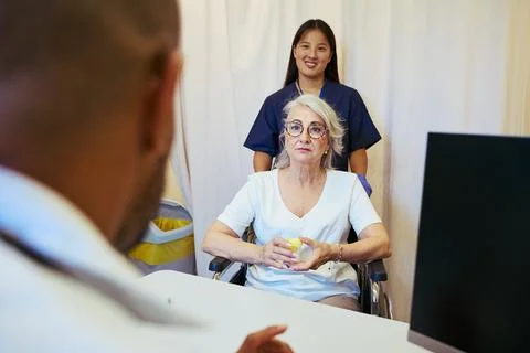 Doctors and nurses providing support to senior woman in wheelchair during Stock Photos