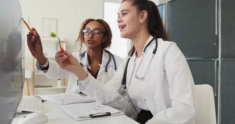 Doctors collaborating at computer in clinic reviewing electronic patient records Stock Footage 344008730