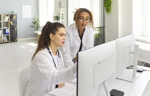 Doctors collaborating at computers reviewing patient records in clinic office Stock Photos