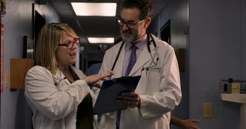 Doctors consulting on a case while a medical assistant checks in another patient Stock Footage 102349405