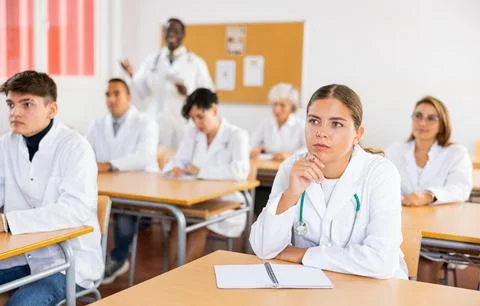 Doctors different age sitting at desk in classroom working during lesson at Stock Photos
