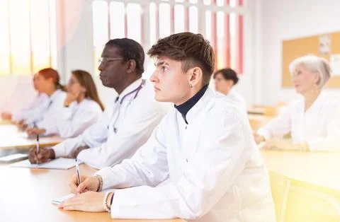 Doctors of different ages sit at their desks and listen carefully to teacher in Stock Photos