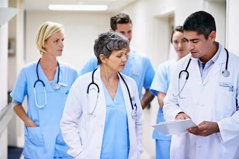 Doctors, explaining and people with paperwork in hallway, help or health service Stock Photos