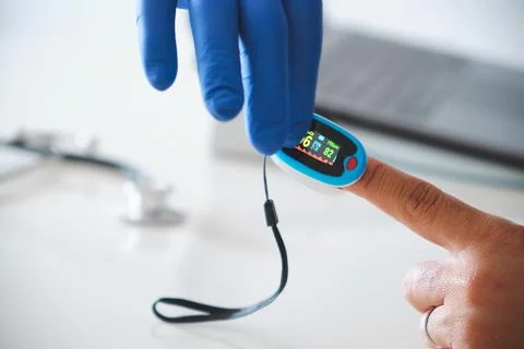 Doctor's gloved hand using pulse oximeter on a finger, monitoring health data Stock Photos
