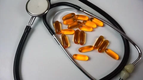 Doctor's hand picking up a fish oil capsule from a pile near a stethoscope on a Stock Footage 333771940