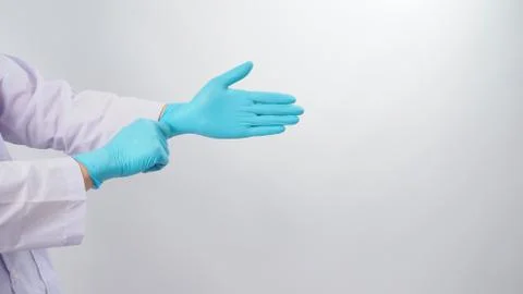 Doctor's hand is pulling blue latex gloves on white background. Stock Photos
