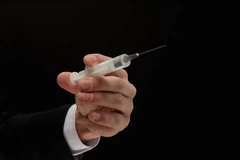 Doctor's hand in a suit holds a syringe with a preparatory stream from the Stock Photos