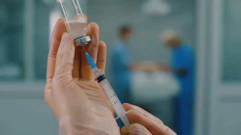 Doctor's hands fill syringe with liquid medicine from vaccine glass bottle Stock Footage 128713468