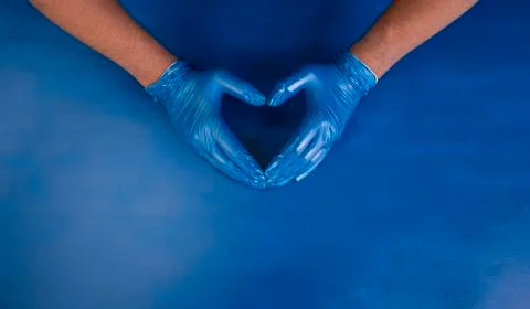 Doctor's hands making heart shape with hands in rubber medical gloves on blue Stock Photos