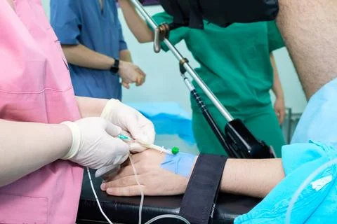 The doctor's hands in sterile gloves insert the needle into the patient's arm. Stock Photos