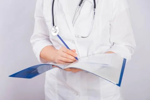 Doctor's hands in a white coat hold a folder and fill out a medical document Stock Photos