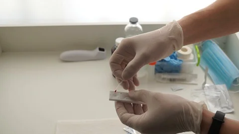 The doctor's hands in white gloves drip a drop of blood on an rapid coronavirus Видео 128767311