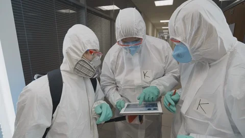 Doctors in hazmat suits and masks using tablet pc in empty building Stock Footage