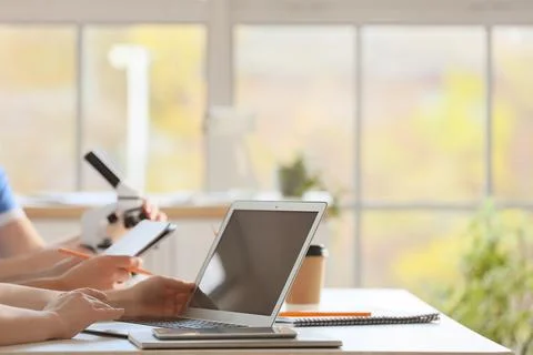 Doctors with laptop and microscope working at table in clinic, closeup Stock Photos