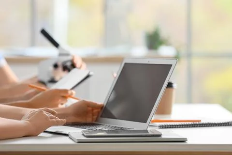 Doctors with laptop and microscope working at table in clinic, closeup Photos