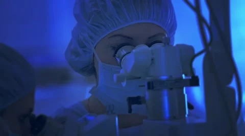 Doctors looks through a microscope during surgery, microsurgery, CINEMATIC BLUE Stock Footage 51445747